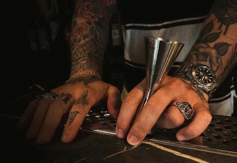 Le mani tatuate del proprietario al bancone mentre prepara un cocktail